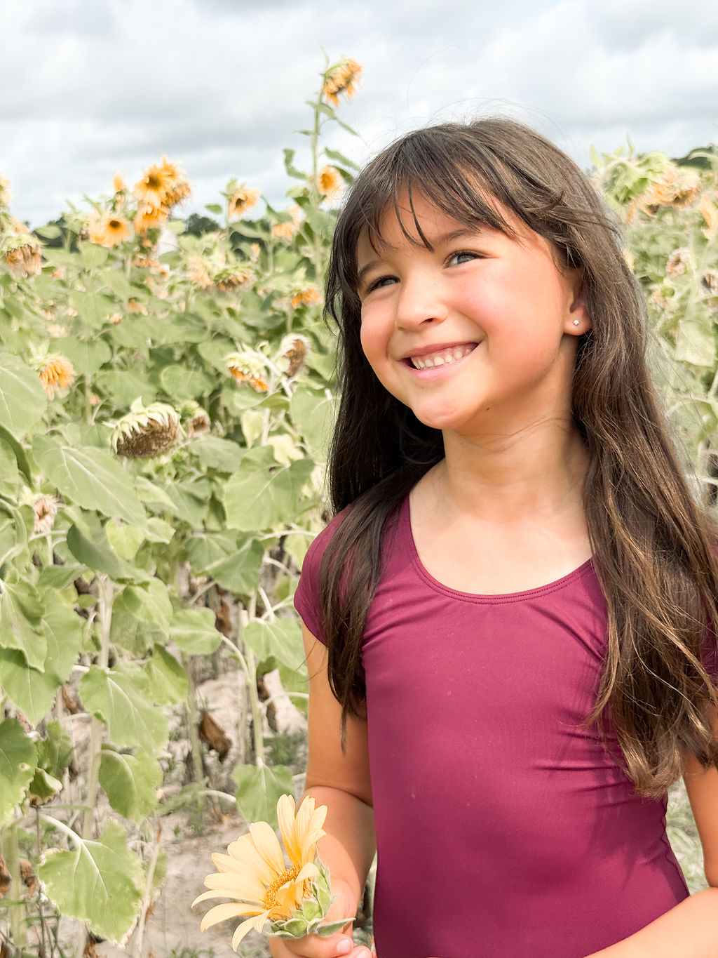 A young dancer smiling beside a sunflower