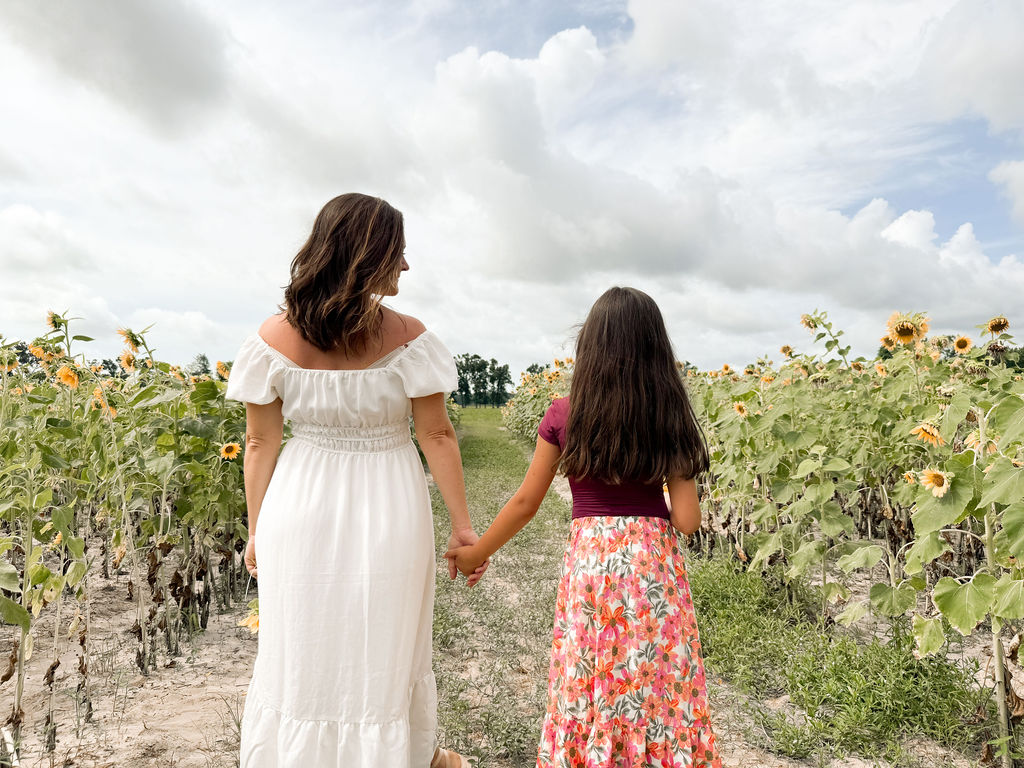 A woman and a girl walking hand in hand down a sunflower row