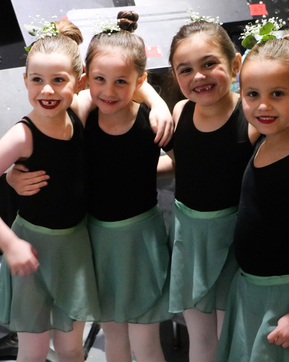 Four young dancers arm in arm in matching sage skirts