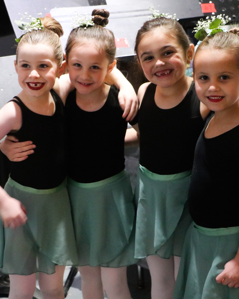 Four company dancers arm in arm backstage before a performance