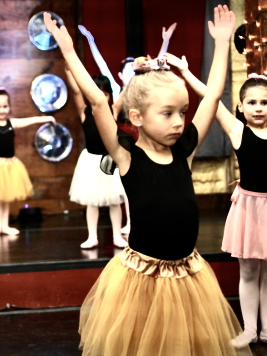 Young dancers with their arms lifted on stage at the fall recital