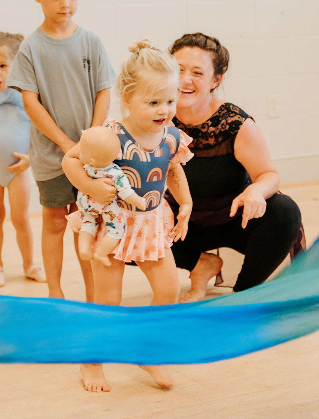 An instructor kneeling with a small group of young dancers around a length of blue silk