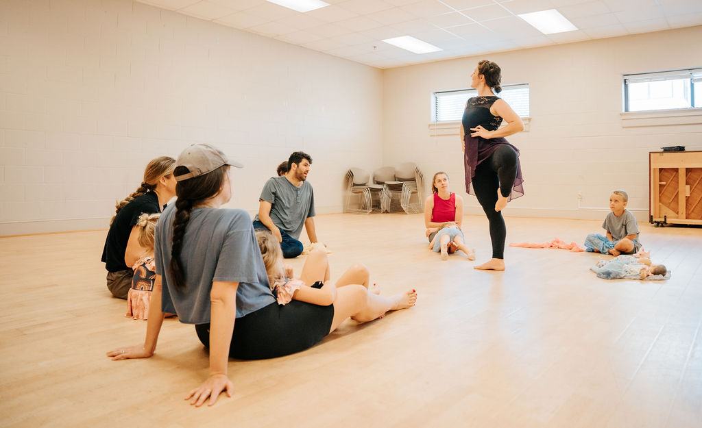 A group seated on the floor watching an instructor lead a worship dance session