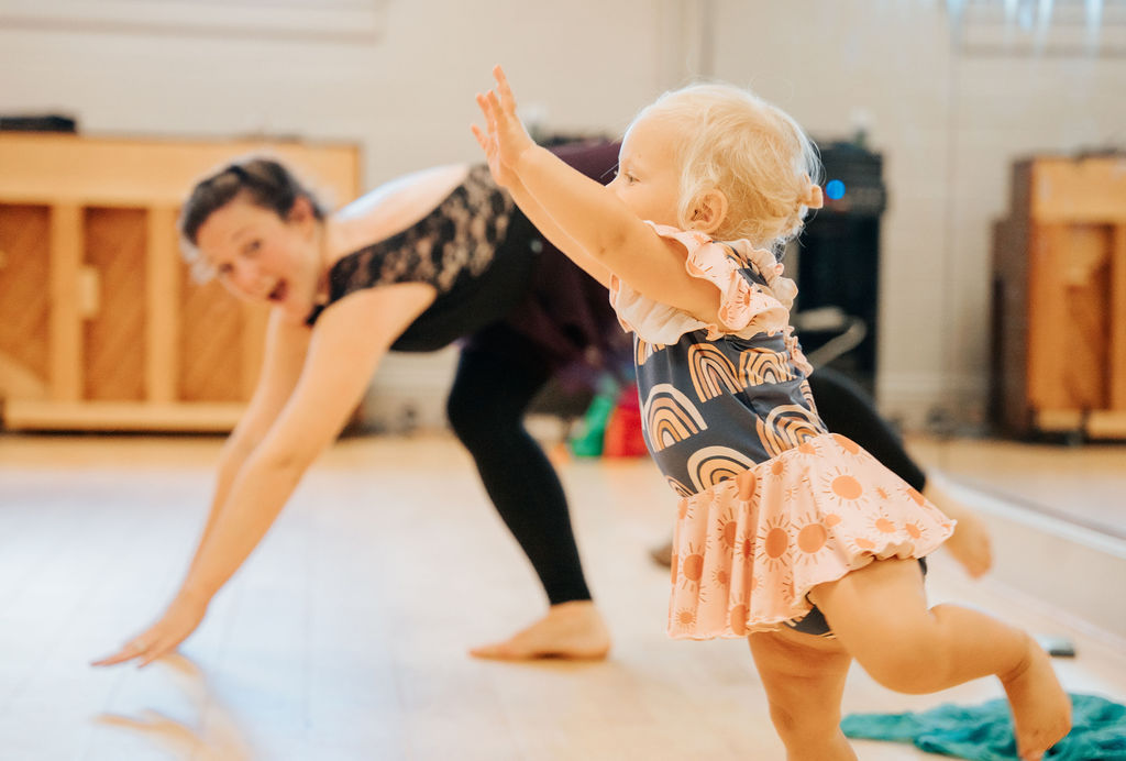 A teacher and a small dancer reaching up together