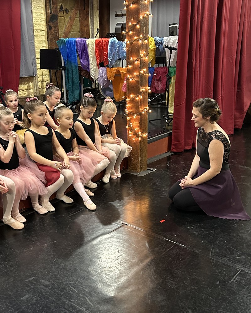 Our founder kneeling in prayer with a class of young dancers before a performance