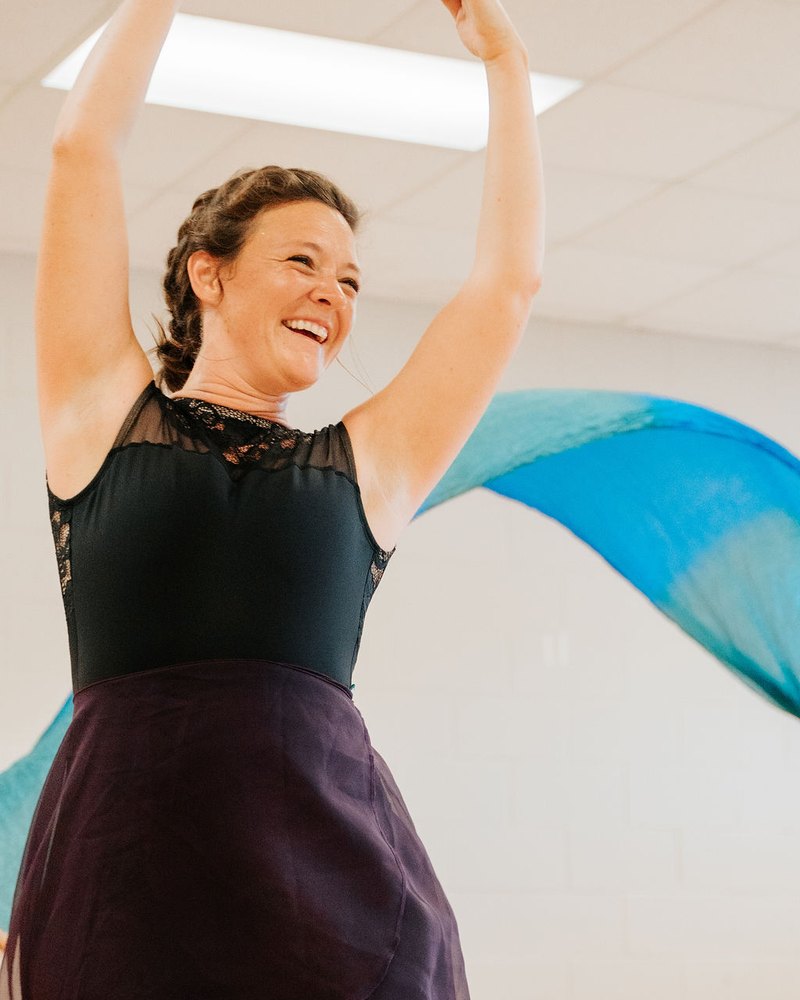 A woman laughing mid-movement with a blue silk swirling behind her