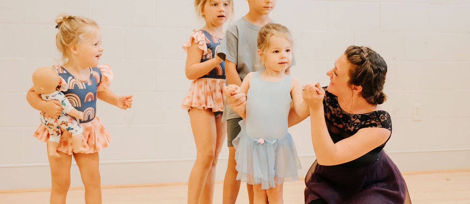 An instructor kneeling with a row of young dancers in class