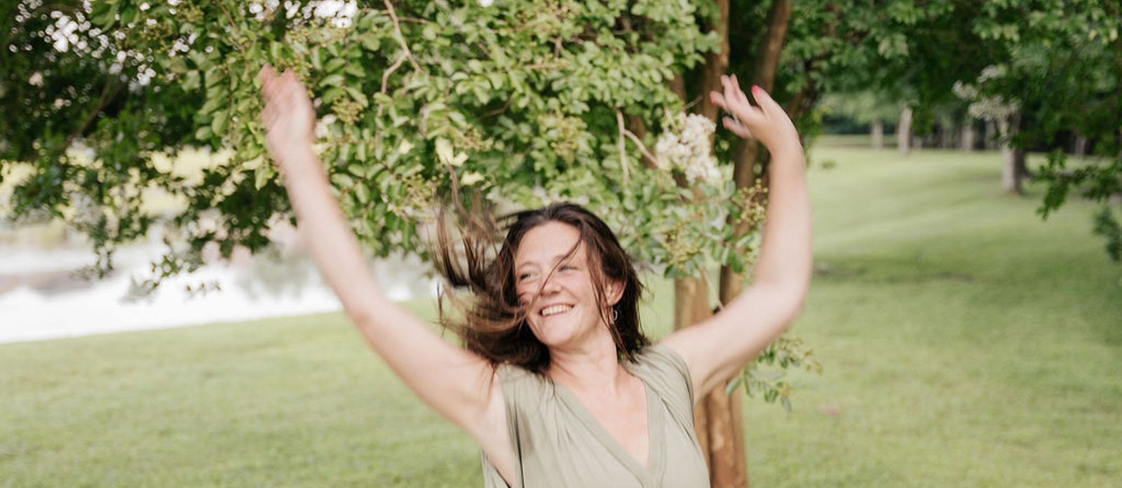 A dancer laughing with her arms lifted on a sunlit lawn