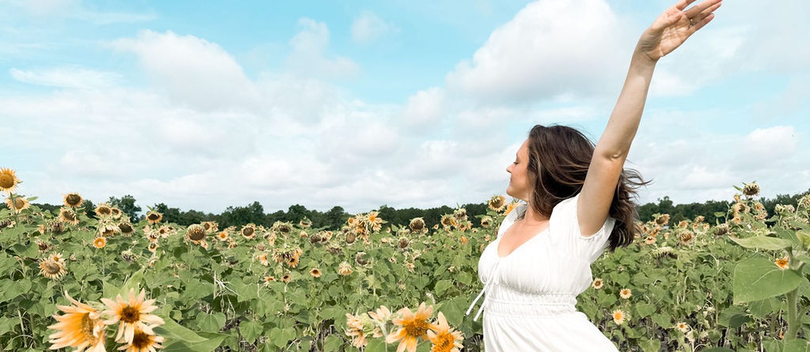 A woman with both arms thrown wide in a sunflower field under an open sky